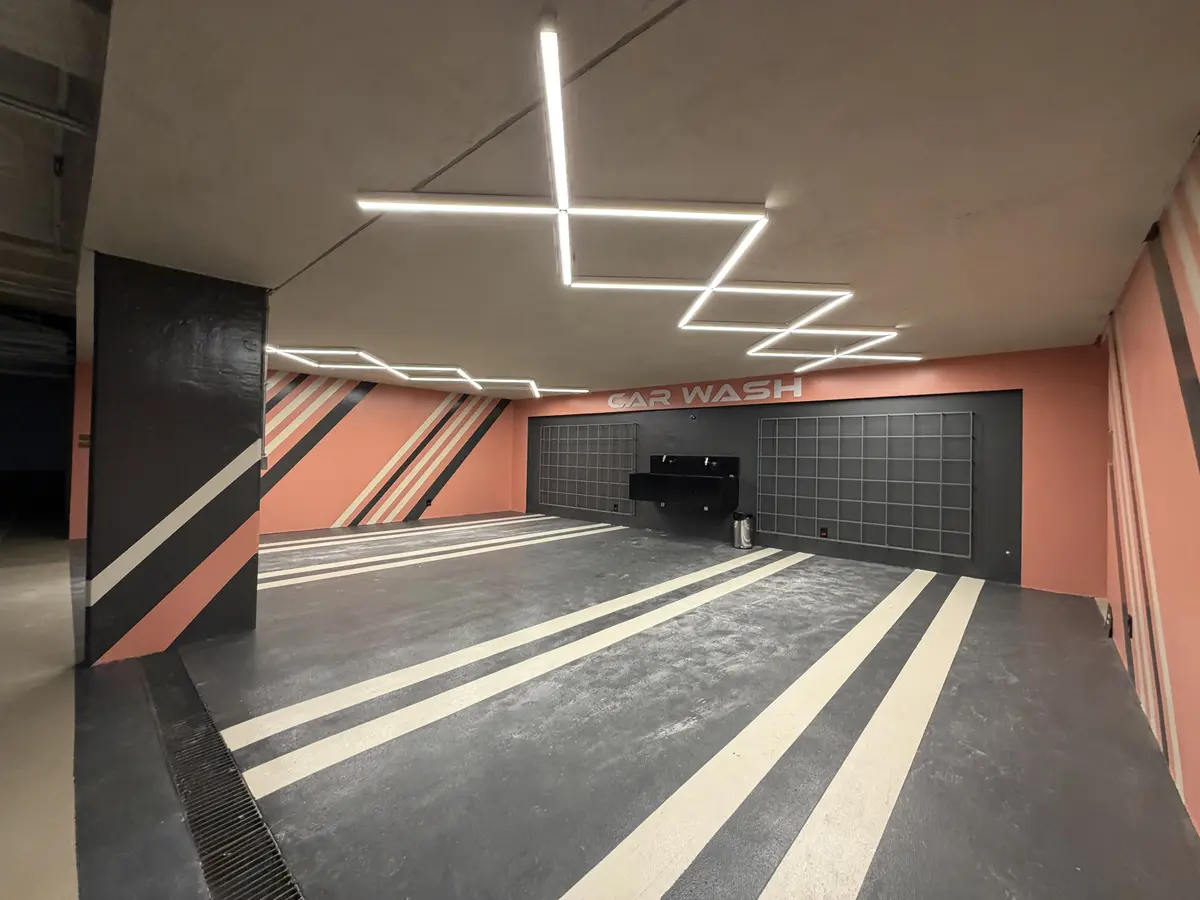 Car wash do Florà Alphaville no subsolo, com piso cinza demarcado por faixas claras, paredes em tom salmão com listras diagonais, bancada de lavagem preta e grades de apoio na parede