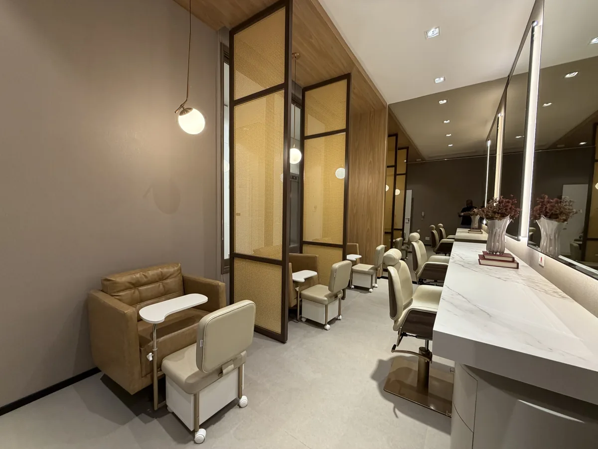 Espaço beauty do Florà Alphaville com poltronas de manicure e pedicure, divisórias de palha com moldura de madeira, pendentes e bancada clara com espelhos iluminados