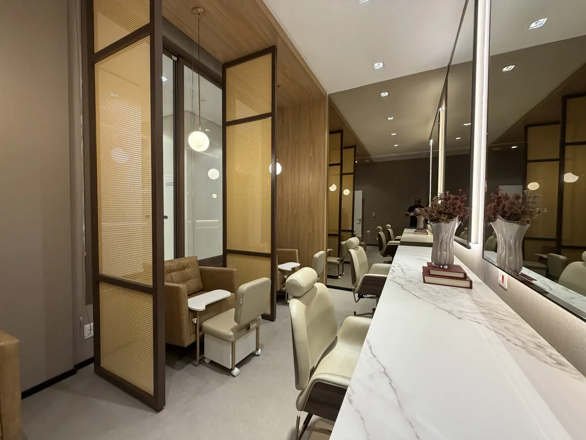 Espaço beauty do Florà Alphaville visto da entrada, com cadeiras de salão, divisórias de palha, estações de pedicure e bancada de atendimento com espelhos