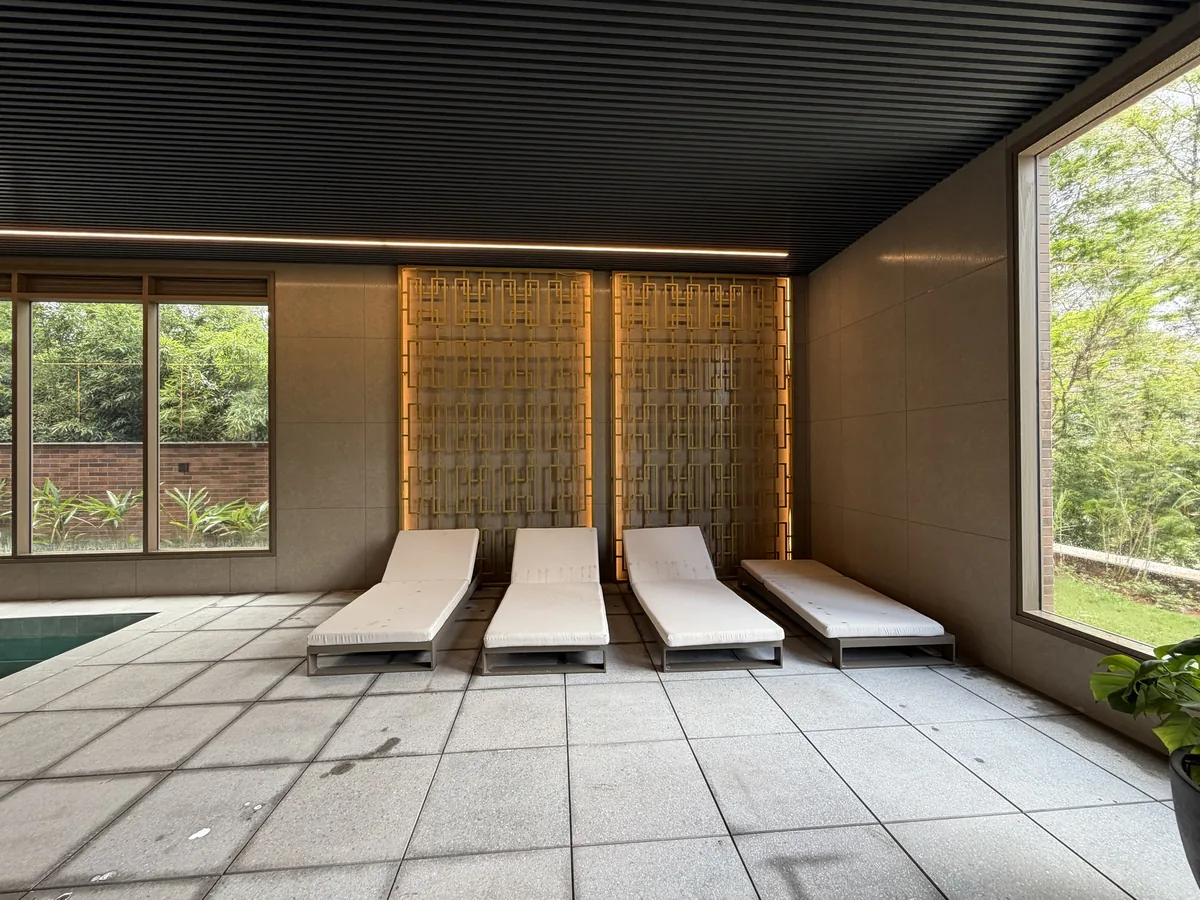 Quatro espreguiçadeiras com colchonete claro diante de painel metálico vazado e retroiluminado, ao lado da piscina coberta do Florà Alphaville