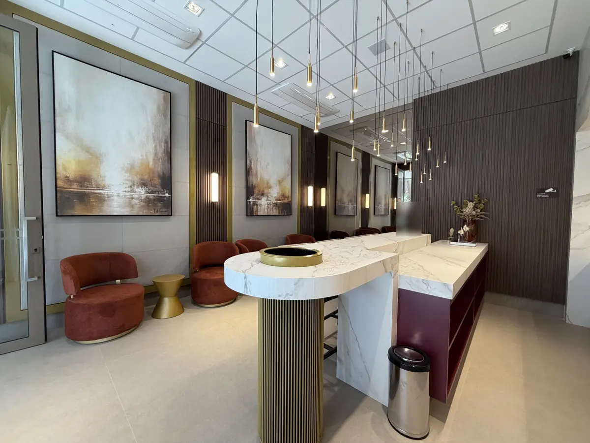 Ambiente social do Florà Alphaville com poltronas giratórias cor de telha, mesa lateral dourada, quadros abstratos, painéis ripados, pendentes dourados e bancada de porcelanato com coluna ripada