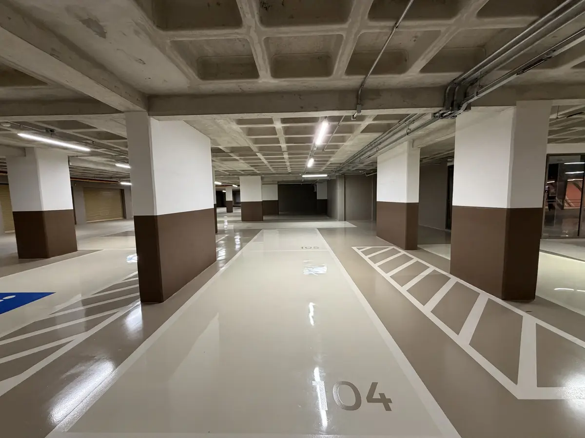 Garagem do Florà Alphaville com vagas numeradas, piso claro em resina, pilares pintados em branco e marrom, faixas de sinalização e vaga de acessibilidade em azul ao fundo