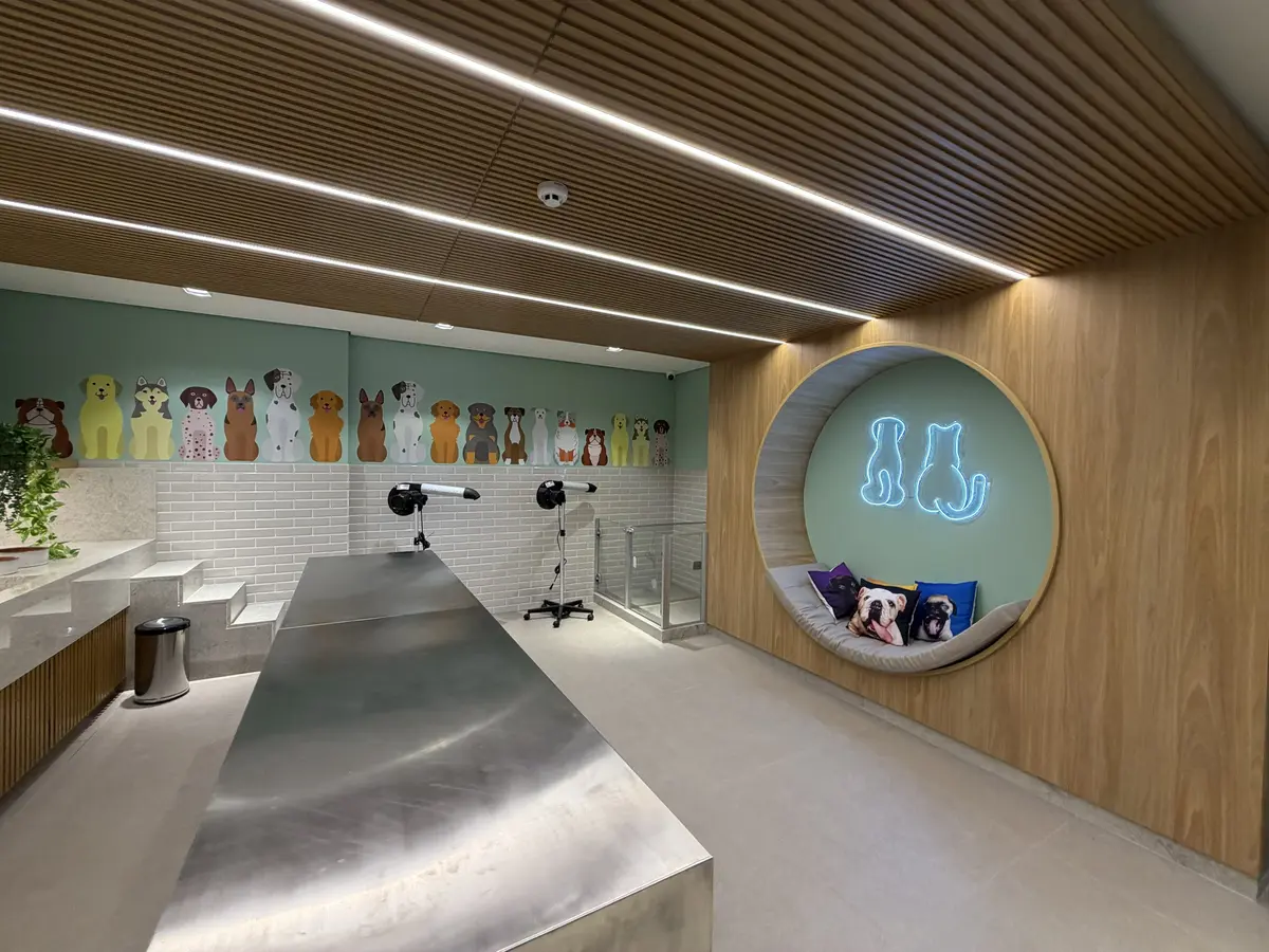 Pet care do Florà Alphaville com mural de cães na parede verde, mesa de inox, dois secadores e nicho circular com neon de cão e gato e almofadas
