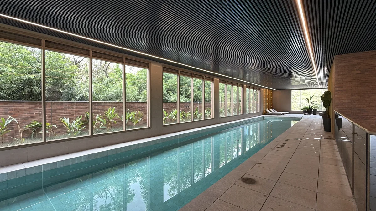 Piscina coberta do Florà Alphaville, comprida, com janelas do piso ao teto voltadas para o jardim de bambus, forro ripado escuro com fita de luz e espreguiçadeiras ao fundo