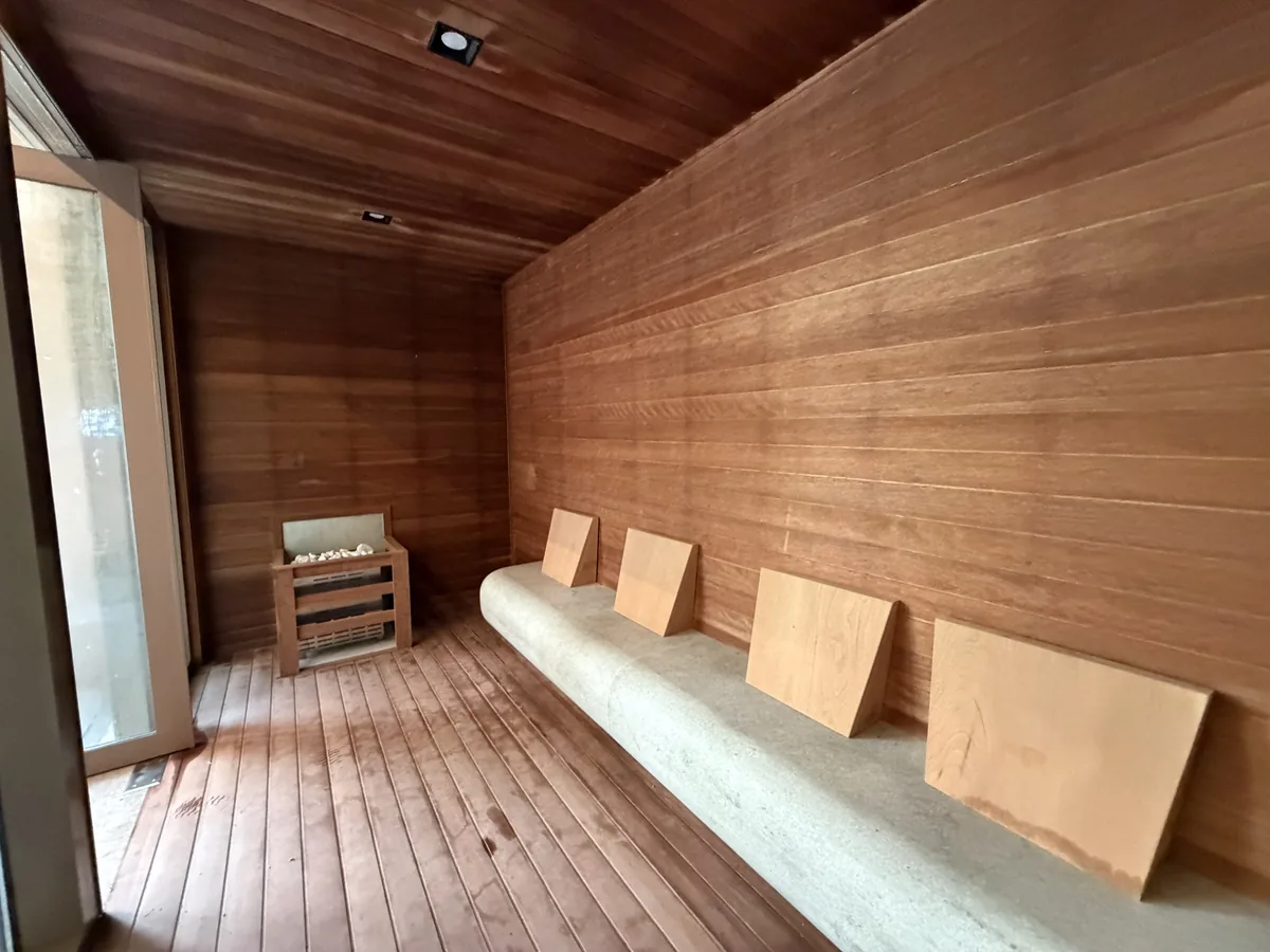 Sauna seca do Florà Alphaville revestida de madeira, com banco de pedra, encostos de madeira e aquecedor com pedras